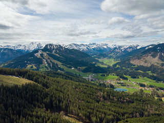 Fototapeta premium Snowy mountains of the Allgäuer Alpen by aerial - drone view on a party cloudy and sunny day with green trees on the foreground