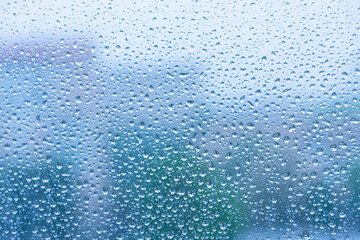 Pattern of moisture and droplets on a window on a rainy cold day. On the background are visibile the blurred profiles of residential buildings.