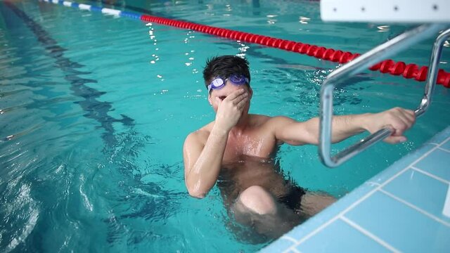 Young positive happy male swimmer in blue water swimming pool after race.