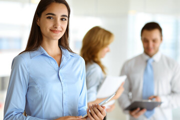 A friendly young dark hair businesswoman or female student is standing with some papers in the office
