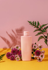 Obraz na płótnie Canvas Summer style of showcase for cosmetics product display on yellow and pink background with flowers. Pink bottle cosmetics product with flowers