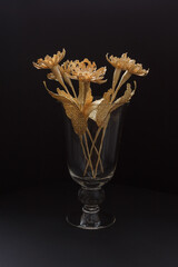 A glass vase with a bouquet of flowers made from straw 
