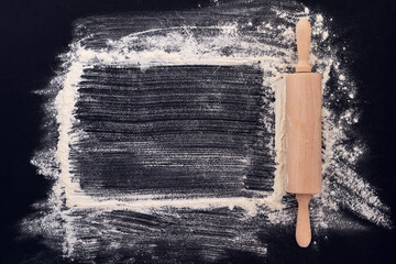 Wooden rolling pin in hands and flour. Bakery on a black stone Top view.