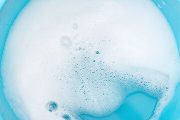 Foam on surface of water in blue plastic basin. Foam as texture or background.