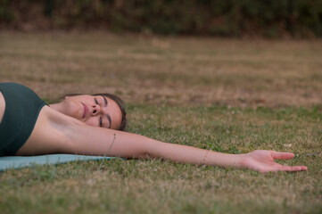 Caucasian woman stretches her arm doing yoga outdoors.