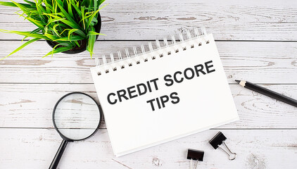 CREDIT SCORE TIPS text concept write on notebook with office tools on the wooden background