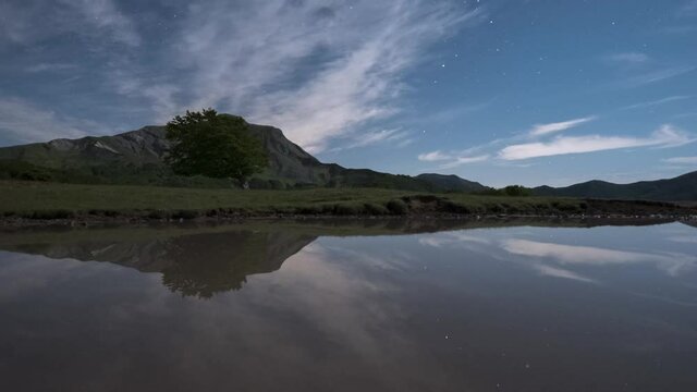 Night time lapse of a mountain landscape, a bent tree and stars perfectly reflected in a lake, Emilia Romagna, Italy, Europe