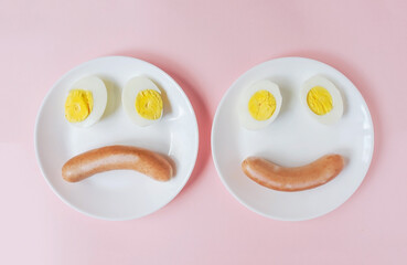 cut boiled eggs with sausage on a plate in the form of a happy and sad smiley face