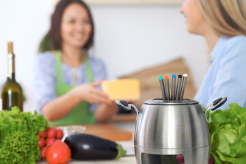 Fondue in a pot at the background of friends cooking together, close-up. Kitchen interiors and cookware