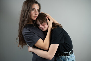 Concept of family support and trust. Mom hugs and comforts teenage daughter on gray background