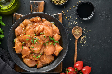 Raw chicken meat marinated in teriyaki soy sauce, onions and pepper in a black plate on a dark slate, stone or concrete background. Top view with copy space.