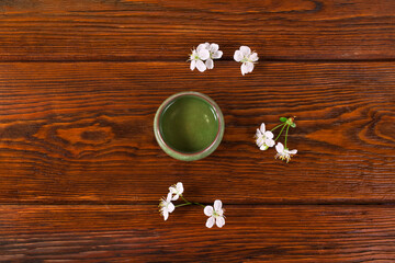 Green tea in a ceramic cup with cherry flowers on a wooden background. Top view.