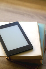 Stack of old hardcover books and e-reader on a table. Selective focus.