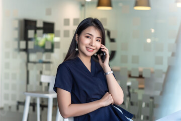 Beautiful Asian woman looking at the camera talking on the phone and sitting on a chair.