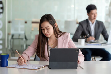 Front view of a beautiful Asian businesswoman holding a pencil with documents a tablet placed at the office.