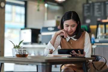 Asian woman sitting in a café spending free time relaxing by tablet at the café.
