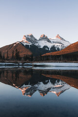 Three Sisters Peak in Canmore, Alberta with their reflection visible on a lake in the foreground