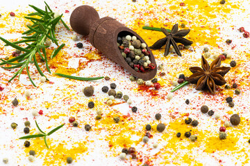 A wooden spoon with a mixture of peppers lies on a background of scattered spices and rosemary.