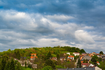 Fototapeta na wymiar Heavy, rainy clouds over the green hill with houses. Beautiful countryside scenery.