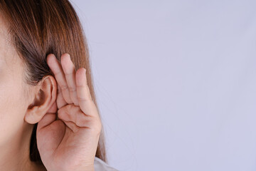 woman hearing loss or hard of hearing and cupping her hand behind her ear isolate grey background,...