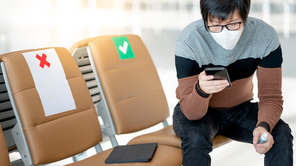 Asian man tourist wearing face mask using smartphone in airport terminal. Coronavirus (COVID-19) pandemic prevention when travel abroad. Health awareness and social distancing