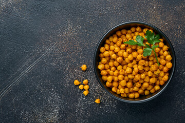 Fried chickpeas with turmeric with parsley and lime in black plate on an old black table background. Roasted spicy chickpeas or Indian chana or chole, popular snack recipe. Top view.