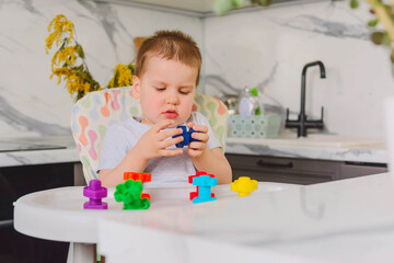 Child boy 2 y.o. plays with plastic colored shaped large screws and nuts, learning through the game.