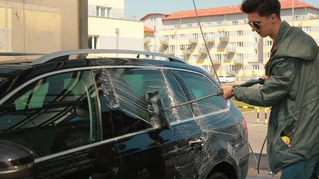 Looks at the paint of vehicles washes away dirty spots. The man washes the car with his hands. He uses a brush and soap. 