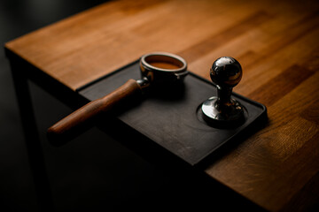 Obraz na płótnie Canvas portafilter with tamped coffee and temper lying on black stand on wooden table