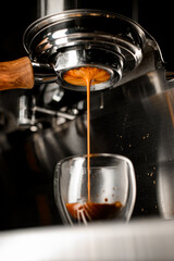 Coffee machine pouring hot espresso in double wall glass from bottomless naked portafilter.