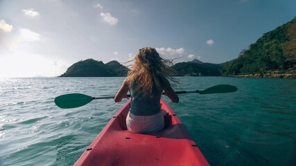 Silhouette of woman tourist raising hands while sailing in canoe along sea bay water to distant...