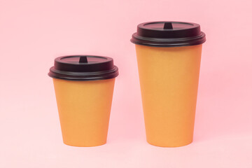 Two brown craft paper cups small 0,3 l and big 0,5 l with black lids of tea or coffee isolated on a pink background. Mockup with empty copy space for text or design. Recycling eco-friendly concept