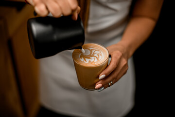 close-up of beautiful glass with coffee in woman's hand into which milk poured from jug