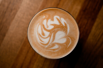 top view of glass of hot coffee with beautiful latte art on wooden table background.