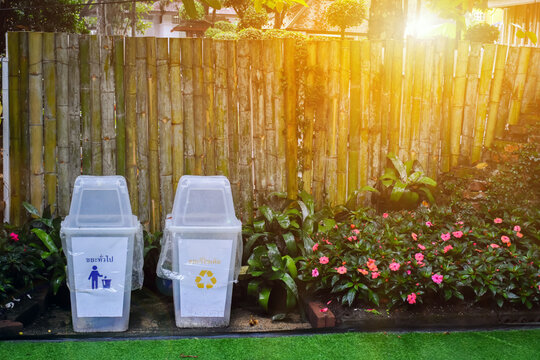 White plastic bins placed in front of the bamboo wall in public park. Thai language on bins means general waste and recyclable waste in English.