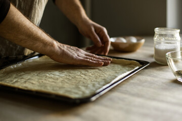 Fototapeta na wymiar Male hands spreading the dough on a baking sheet