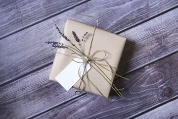 Present wrapped in natural brown paper with lavender flowers and name tag on wooden background. Natural eco friendly packaging. Zero waste gift wrapping idea.