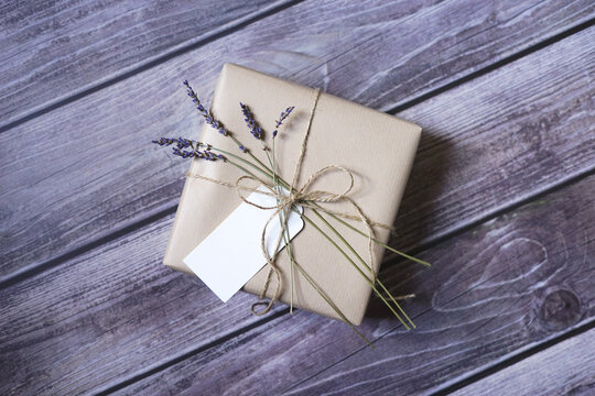 Present wrapped in natural brown paper with lavender flowers and name tag on wooden background. Natural eco friendly packaging. Zero waste gift wrapping idea.