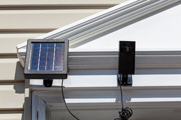  a wireless security surveillence camera with motion sensor on top of the front door frame. The camera is linked to a solar panel for environmental friendly charging.