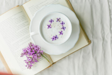 Obraz na płótnie Canvas Mug of cappuccino on a beige background. Lilac flowers, book. Rest at home. Quarantine.