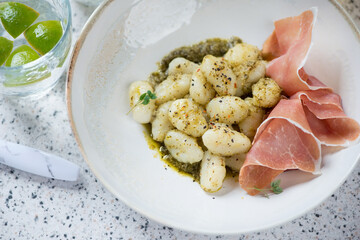 Italian gnocchi served with basil pesto sauce and prosciutto ham in a beige plate, elevated view, closeup