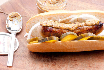 Closeup shot of a hot dog with onions and pickles and a spoon next to a jar of sauce
