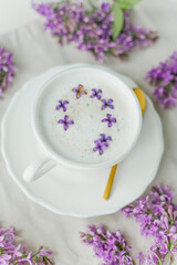 Mug of cappuccino on a beige background. Lilac flowers. Rest at home. Quarantine.