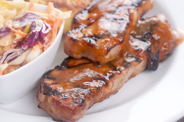 Closeup shot of a two pieces of stake with sauce and a bowl of salad on a white plate