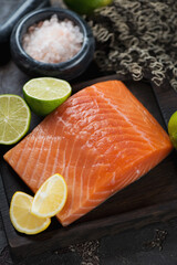 Close-up of raw salmon fillet with pink salt and limes, vertical shot, selective focus