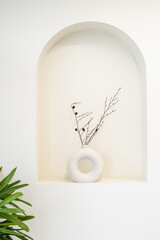 Cotton flowers in a white ceramic round vase on an abstract windowpane against a white wall
