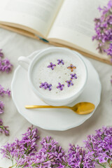 Obraz na płótnie Canvas Mug of cappuccino on a beige background. Lilac flowers, book. Rest at home. Quarantine.
