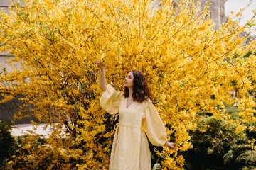 Young woman in a summer dress, on a yellow bush background, outdoors in a garden.