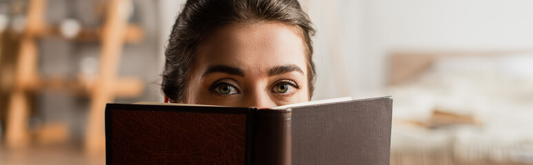 woman obscuring face while holding book and looking at camera, banner