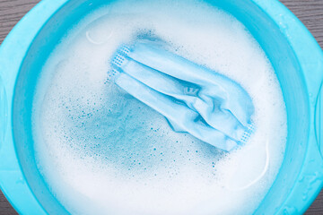 Disposable medical mask soaking in blue plastic basin with water with foam for second use, concept picture about virus and protection